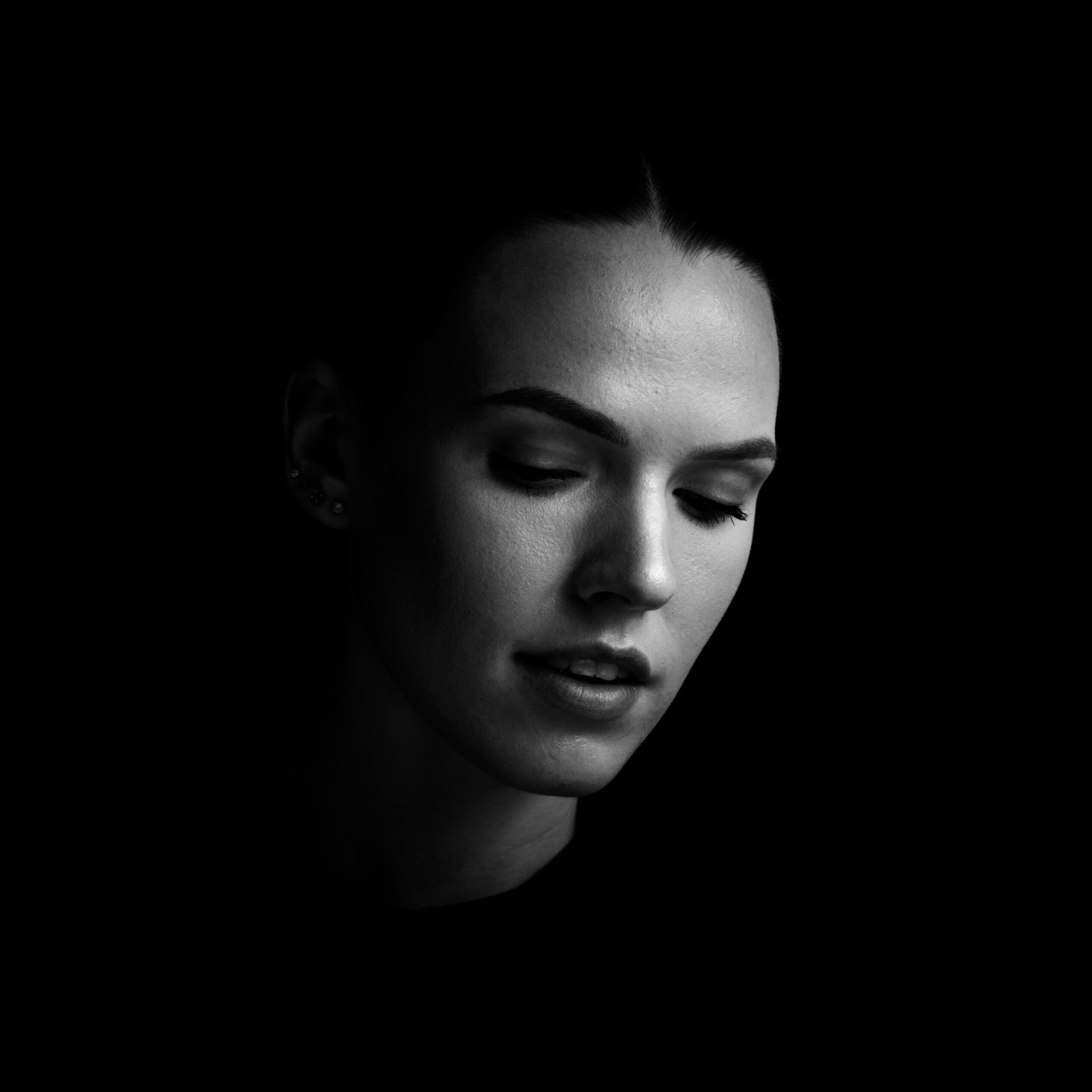 Black and white close up photo of Antonina Klein looking down in front of a black background. Self-portrait.