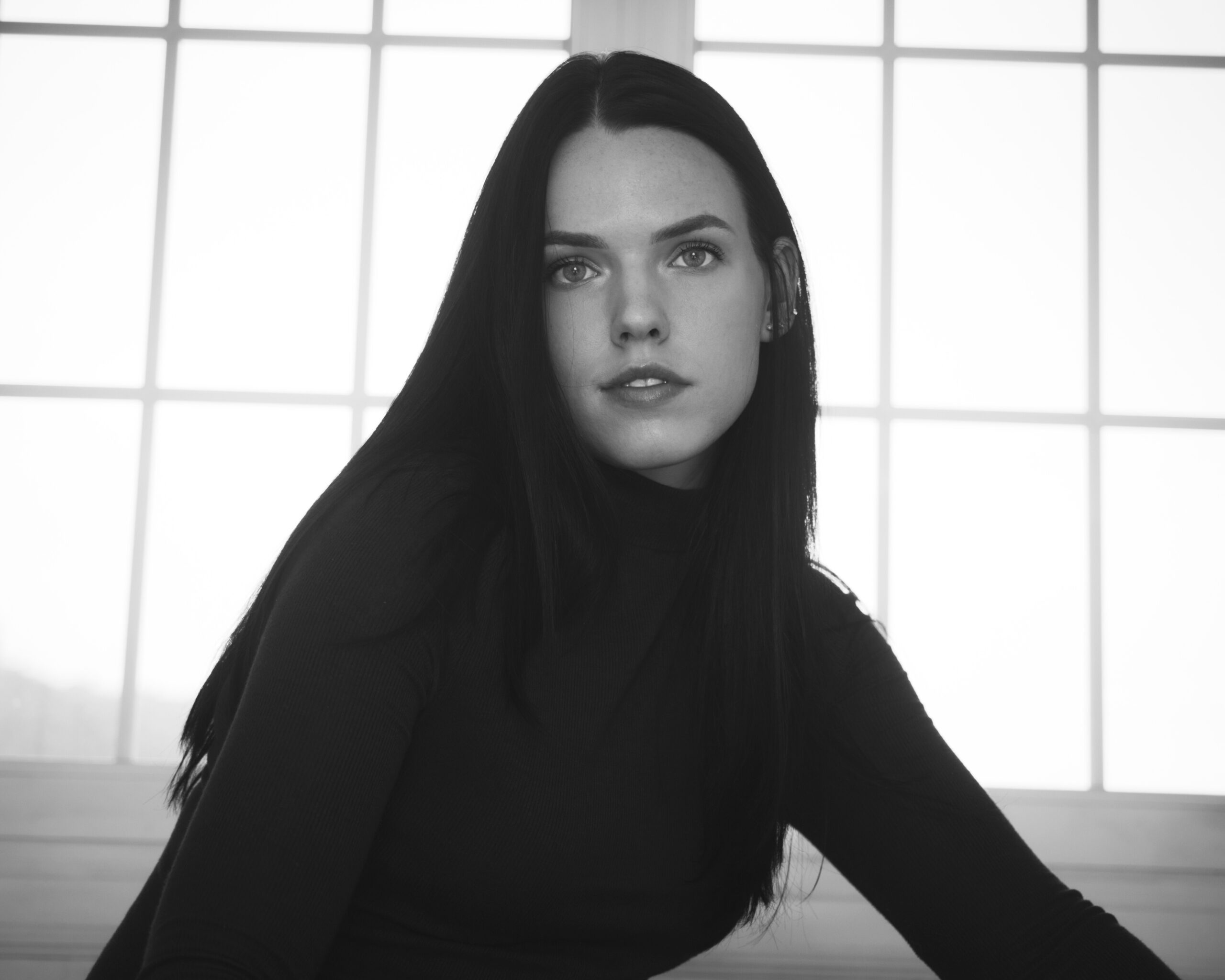 Black and white photo of Antonina Klein looking directly at the camera while sitting in front of a white window.