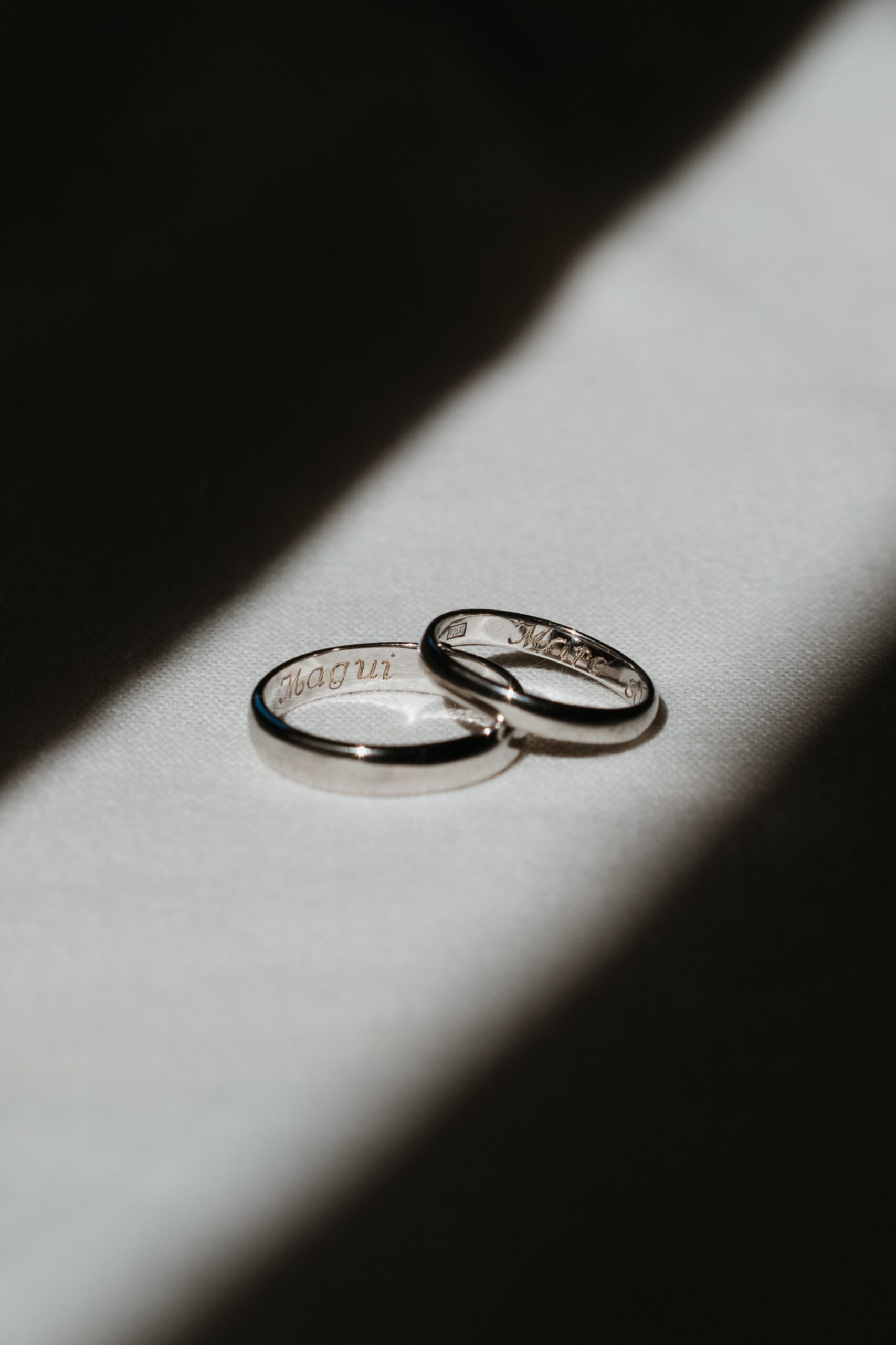 Close up photo of two wedding bands laying on a white cloth under a ray of light with engravings on the inside.