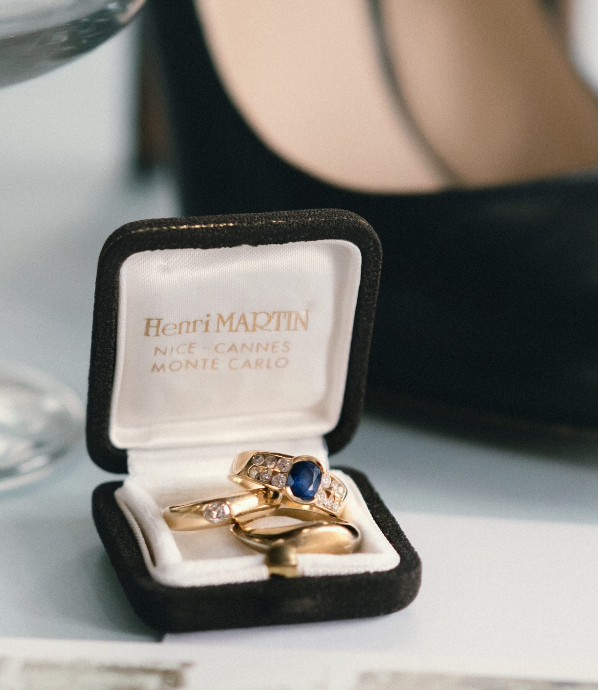 Close up details photo of three wedding rings with diamonds and a blue sapphire in a vintage black velvet ring box from France's Henri Martin in Nice Cannes and Monte Carlo