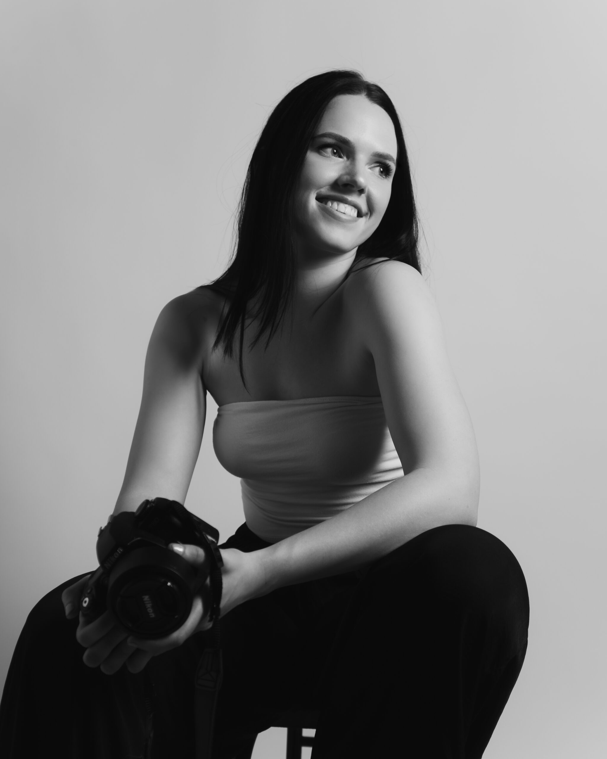 Black and white photo of Antonina Klein in a studio in front of a white backdrop holding a camera and looking away.